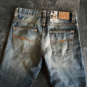 Nudie Jeans Straight Alf blå jeans - Säljer ett par Nudie Jeans Straight Alf i tvätten Org. Cloudy Vintage. Klassiska blå jeans med snyggt slitna detaljer, raka ben och kontrastsömmar. Bakfickorna har Nudie Jeans signaturbrodyr. Perfekta för dig som gillar en avslappnad men stilren look.