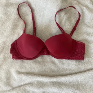 Röd spets-bh från Calvin Klein EU 75A - Snygg röd bh från Calvin Klein med vadderade kupor och spetsdetaljer på sidorna. Axelbanden är justerbara och har Calvin Klein-logga. Perfekt för dig som gillar en mix av stil och komfort.
