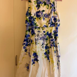 Blommig långklänning från Ralph Lauren - Superfin långklänning från Lauren Ralph Lauren med blommigt mönster i blått, grönt och gult på vit botten. Ärmlös modell med vacker omlottliknande detalj upptill och dragkedja i sidan. Perfekt för sommarens alla tillfällen!