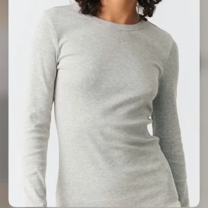 Ljusgrå ribbad långärmad tröja Gina Tricot - En basic ljusgrå långärmad tröja från Gina Tricot, Basically Basics-kollektionen. Tröjan är ribbad, har rund halsringning och sitter figurnära. Perfekt att styla med jeans eller kjol för en clean look.