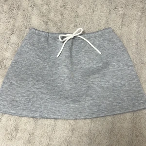 Grå kortkjol med snörning från Gina Tricot - Superenkel och snygg gråmelerad kortkjol från Gina Tricot i mjukt material. Kjolen har en vit snörning i midjan. Kjolen har prislapp kvar. Ställ frågor om du har och priset kan också diskuteras.