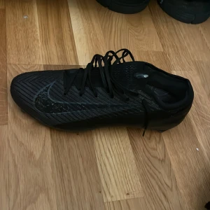 Svarta Nike Mecurials vapor Elite 16 storlek 44 - Säljer ett par helsvarta Nike fotbollsskor med snygg, modern design. Skorna har snörning, mönstrad ovandel och rund tå. Tillverkade i syntetmaterial för bästa grepp och känsla på planen. Perfekta för dig som vill ha stilrena och funktionella skor till matchen. Använda men inte slitits mycket. Mycket bra skick! Nypris 3399