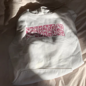 Vit hoodie från Puma med rosa tryck - Vit hoodie från Puma med stor rosa logga framtill i leopardmönster. Tröjan har huva med snörning och en klassisk känguruficka. Mjuk insida och ribbade muddar vid ärmslut och nederkant. Perfekt för dig som gillar sportig och trendig stil.