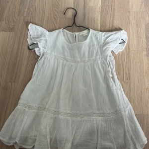 Vit somrig blus från Gina Tricot - Supersöt vit blus från Gina Tricot med volangärmar och fina spetsdetaljer. Blusen är luftig och har en lätt, flowy känsla – perfekt för varma dagar. Tillverkad i ett tunt, mjukt material som känns skönt mot huden.