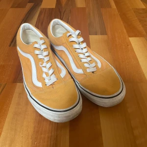 Vans - Snygga Vans Old Skool sneakers i gul och vit med klassisk vågig sidodetalj. Skorna har vit snörning, platt sula och är tillverkade i canvas och mocka. Använda några gånger, och är därmed missfärgade på sidorna. 