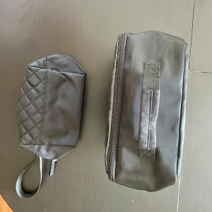 Svarta necessärer med quiltad detalj - Två svarta, enkla necessärer i syntetmaterial, båda med quiltad mönsterdetalj och praktisk handrem. Necessärerna har dragkedja. Den större L:26 B:12 H:25, den mindre L:18 B:8 H:13. Aldrig använda. Säljes tillsammans.