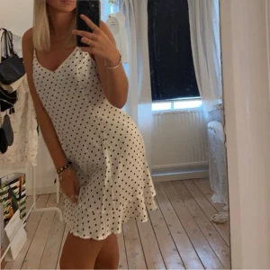 Vit prickig kortklänning - Supersöt vit kortklänning med svarta prickar och v-ringning. Den är i storlek 40 men skulle mer säga att den är som en S. 