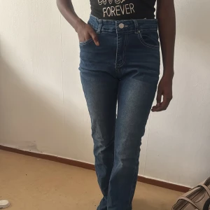 Mörkblå högmidjade jeans med broderi - Säljer ett par mörkblå högmidjade jeans med snygga broderade detaljer på bakfickorna och klassisk femficksdesign. Jeansen har raka ben och stängs med knapp och dragkedja. Perfekta för dig som gillar en stilren men ändå unik look.