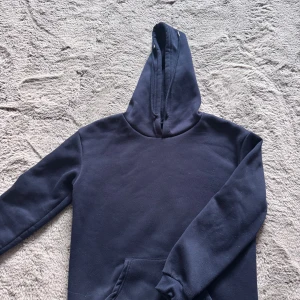 Mörkblå hoodie med huva - En stilren mörkblå hoodie med huva och magficka. Tröjan har långa ärmar och ribbade muddar vid ärmslut och nederkant. Köpt på shein, inte använd så mycket.