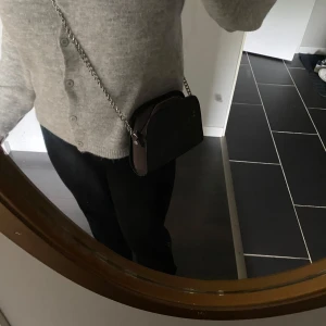 Grå axelremsväska med kedja - Snygg grå axelväska med en silverfärgad kedja som axelrem. Perfekt storlek för det viktigaste.  Mått: 20x15 cm