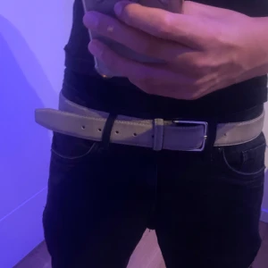 Beige mockabälte med silverfärgat spänne - Snyggt Beige bälte i mocka med stilrent silverfärgat metallspänne. Bältet har en klassisk design med raka kanter och en mjuk yta. Insidan är brun och bältet passar perfekt till jeans eller chinos för en clean look.