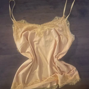 Gul linnetopp med spets från Costercopenhagen - Supersöt gul linnetopp från Costercopenhagen i satinliknande material med tunna axelband och fina spetsdetaljer längs urringning och nederkant. Perfekt för dig som gillar en feminin och trendig look. Sitter snyggt och känns lyxig mot huden.