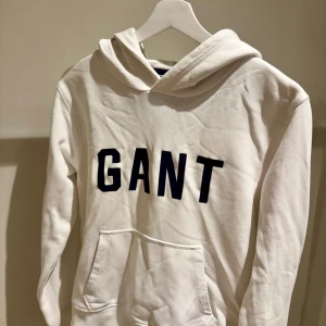 Vit hoodie från GANT med tryck - Säljer en stilren vit hoodie från GANT med svart tryck över bröstet. Storlek 170