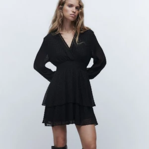 Svart kort klänning från Zara XS - Supersöt svart kort klänning från Zara i storlek XS. Klänningen har v-ringning, långa transparenta ärmar och volangkjol i två lager. Prickigt mönster i tyget och markerad midja ger en snygg siluett. Perfekt för dig som gillar trendiga detaljer!