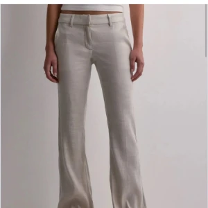 Beiga lågmidjade linnebyxor med bootcut - Helt nya, prislapp kvar. Snygga beiga linnebyxor eller kostymbyxor med bootcut-snitt och låg midja. Byxorna har hällor för bälte och stängs med dragkedja och knapp. Perfekta för en clean och stilren look. Köpta för 500, slutsålda i denna storlek.