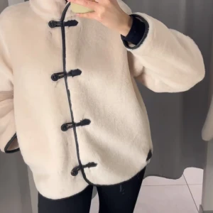 Beige teddyjacka med svarta detaljer - Säljer en beige teddyjacka med svarta kantband och coola knäppningar framtill. Jackan har hög krage, loose passform och är långärmad. Perfekt för dig som vill ha en mysig och trendig look under höst och vinter.