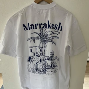 Vit t-shirt med Marrakesh - Säljer en vit t-shirt från YOURTURN med ett stort blått Marrakesh-tryck på baksidan och en mindre logga på framsidan. T-shirten är riktigt stilren och passar bra inför sommaren😁Tröjan är XS men passar S