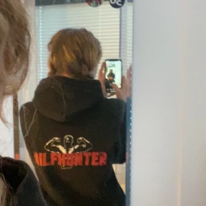 Svart hoodie från Revenite - Säljer en svart hoodie från Revenite med texten 'MILFHUNTER' i rött på ryggen. Hoodien har en klassisk design med huva och långa ärmar. Använd några gånger men i perfekt skick