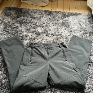 Grå täckbyxor i polyester - Säljer ett par grå täckbyxor i 100% polyester. Byxorna har dragkedjor vid fickorna och elastisk midja för extra komfort. Perfekta för kyliga dagar.