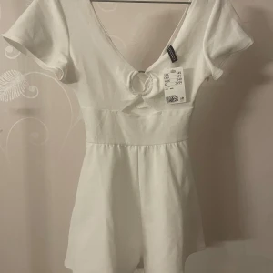  Byxdress  - Säljer en söt vit kort byxdress med v-ringning. Klänningen har korta ärmar och en figurnära passform som passar perfekt för sommarens alla tillfällen.