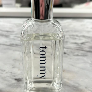 Tommy Hilfiger parfym - Elegant parfym från Tommy Hilfiger med en stilren design. Flaskan är genomskinlig med märkets namn tryckt i blått på framsidan. Korken är silverfärgad med ingraverad text. Perfekt för den som söker en klassisk och tidlös doft.