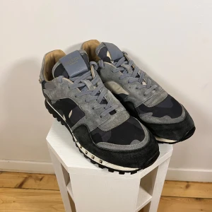 Rockrunners - Snygga sneakers från Valentino i en cool camouflage-design. Skorna har gråa och svarta nyanser med snörning och dekorativa nitar runt sulan. Perfekta för en stilren look med en touch av edge.