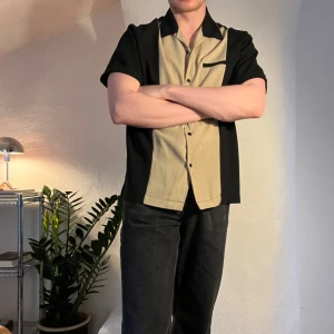 Kortärmad bowling skjorta - Trevlig skjorta med bowlingkrage. Svart å beige på framsidan, helsvart på baksidan. Bra kvalitet, bra skick! Kika gärna andra annonser, samfrakta gärna.
