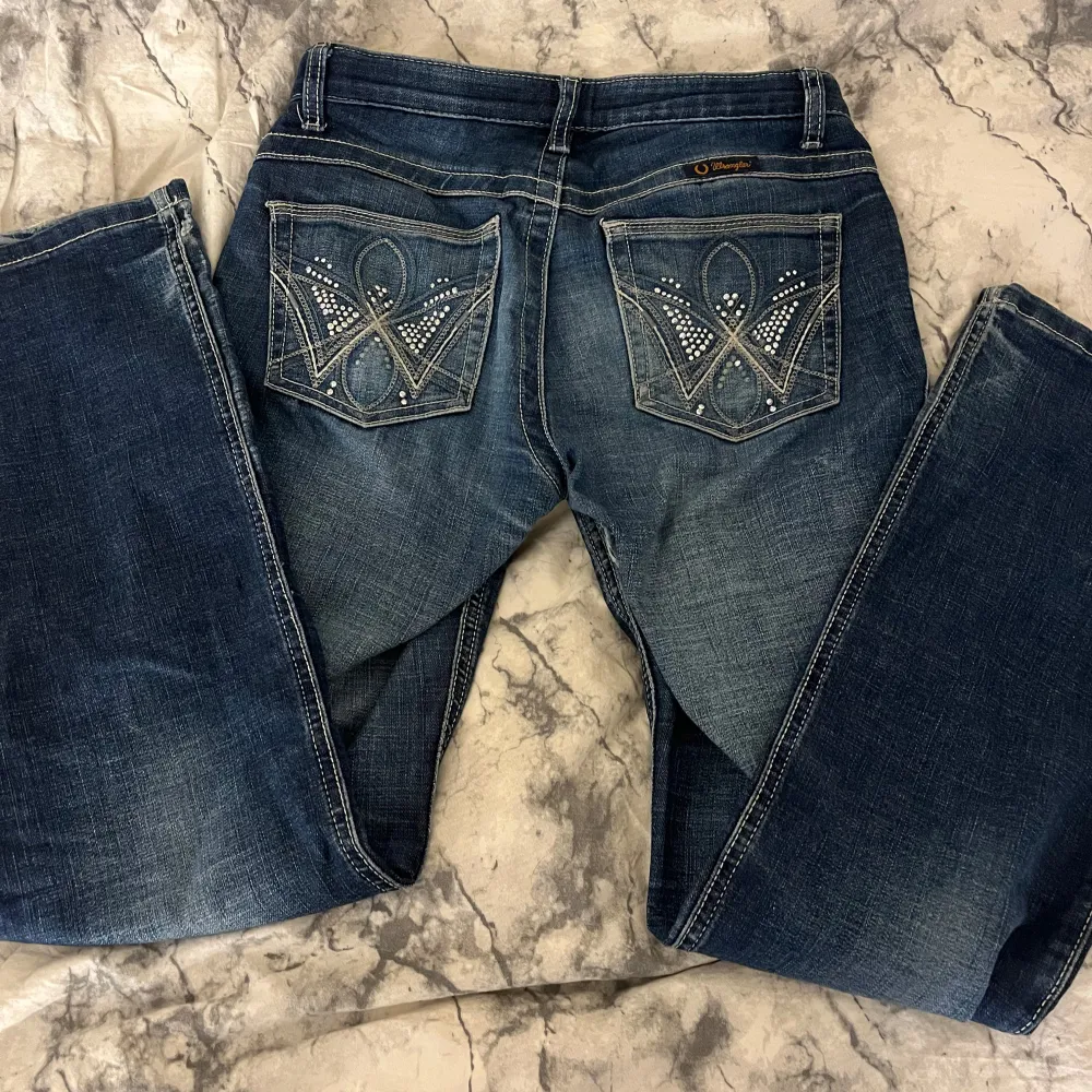 Snygga blå jeans från Wrangler med bootcut-stil. De har dekorativa detaljer på bakfickorna och en klassisk femficksdesign. Perfekta för en avslappnad look. Dem har hål/slitningar vid innerlåren därav priset . Farkut & Housut.