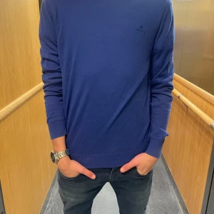 Blå tröja från GANT - Säljer en stilren blå tröja från GANT med rund hals och långa ärmar. Perfekt för en avslappnad och snygg look. Tröjan har en diskret logga på bröstet. Om de är några frågor eller funderingar är de bara att skriva. 