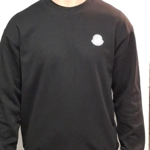 Svart tröja från Moncler - Säljer en stilren svart tröja från Moncler med deras ikoniska logga på bröstet. Tröjan har långa ärmar och en klassisk passform. Perfekt för en avslappnad och trendig look.