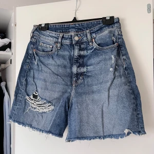 Blå jeansshorts med slitningar - Säljer ett par coola blå jeansshorts från H&M med slitningar och fransiga kanter. Shortsen har en hög midja och klassisk femficksdesign. Perfekta för en avslappnad stil. Använda ca 5 gånger. Önskar du veta exakta mått? Tveka inte att höra av dig!