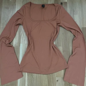 Brun långärmad topp - Säljer en stilren brun långärmad topp. Toppen har en fyrkantig halsringning och är figurnära i passformen.Anvönd fåtal ggr.