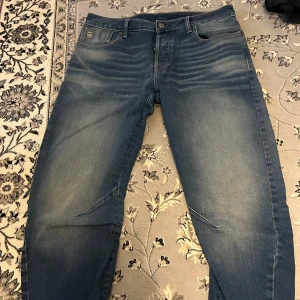 Blå jeans från G-Star RAW - Snygga blå jeans från G-Star RAW med en slim passform. Modellen heter ARC 3D Slim och har en modern design med lätt slitna detaljer. Perfekta för en stilren look. Säljs pågrund av dem blivit för stora på mig. Priset kan diskuteras!