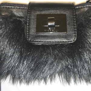 Svart Fiorelli pälsdetaljerad plånbok - Snygg svart plånbok med  Fiorelli  pälsdetaljer och ett stilrent spänne framtill. Insidan är fodrad med lila tyg och har flera fack för kort och mynt. Perfekt för att ge en touch av lyx till din vardag.