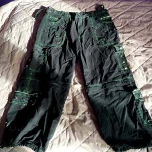 Svarta cargopants med gröna sömmar - Coola svarta cargopants med kontrasterande gröna sömmar och flera fickor. Byxorna har en loose passform och är perfekta för en avslappnad stil. De har även detaljer som knappar och dragkedja.