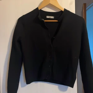 Svart kofta från Gina Tricot - Säljer en stilren svart kofta från Gina Tricot i premiumkvalitet. Koftan har knappar framtill och är perfekt för en elegant look. Den är långärmad och passar bra till både vardag och mer uppklädda tillfällen.den är i storlek S men den kymptes i tvätten så den är som XS (den köptes för 600kr men priset kan såklart diskuteras!)