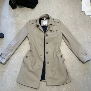 Beige trenchcoat från Tommy Hilfiger - Jätte fin Tommy Hilfiger jacka i bra skick. Jag fick jackan i present men jag säljer den pågrund av att den inte passar min stil. Den saknar bälte men funkar utmärkt utan eller med ett annat bälte. Skriv till mig om du undrar något. Pris kan diskuteras.