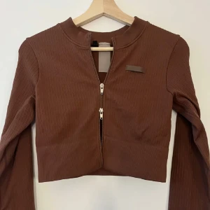 Brun ribbad croppad tröja från Bo+tee - Snygg brun croppad tröja från Bo+tee med ribbad textur och dragkedja framtill. Perfekt för en trendig look med långa ärmar och en stilren design.