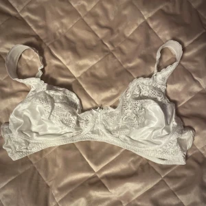 Fin vit Spets BH utan bygel - Säljer en elegant vit bh med spetsdetaljer utan bygel! Den har justerbara axelband och en klassisk design med vackra broderier. Perfekt för att känna sig extra fin och bekväm under kläderna. Storlek 105 D!