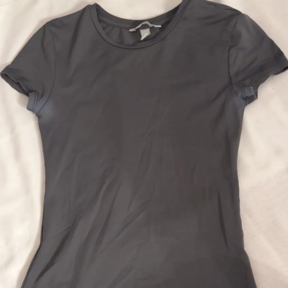 Säljer en stilren grå t-shirt från H&M. Den är kortärmad och har en normal passform, perfekt för en avslappnad look. Materialet känns mjukt och bekvämt mot huden, material som är lite sportigt och likt skims material. T-paidat.