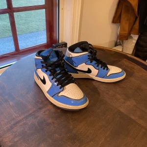 Nike Air Jordans i blått och vitt - Säljer ett par Nike Air Jordans i en snygg blå och vit färgkombination med svarta detaljer. Skorna har klassisk snörning och den ikoniska Nike-loggan på sidan. Perfekta för dig som vill ha en stilren och sportig look.
