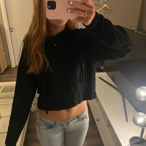 Svart croppad stickad hoodie  - Säljer en svart croppad stickad hoodie med långa ärmar!!💛Perfekt för en avslappnad stil och kan enkelt matchas med jeans eller kjol. Tröjan har en enkel design utan mönster eller detaljer.
