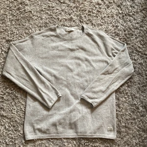 Grå tröja från Jack & Jones - Säljer en stilren grå tröja från Jack & Jones. Tröjan har en klassisk rund hals och långa ärmar, perfekt för en avslappnad look. Tillverkad i ett mjukt material som känns skönt mot huden. Passar bra till både jeans och chinos. Storlek L Man 