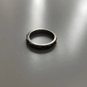 Silverfärgad ring med mönster - Säljer en elegant silverfärgad ring med ett intrikat mönster runt om. Ringen har en klassisk design som passar perfekt för både vardag och speciella tillfällen.