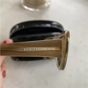 Solglasögon från Dolce & Gabbana - Snygga solglasögon från Dolce & Gabbana med en stilren design. Bågarna är i en elegant beige färg och har en bred form som ger ett coolt intryck. Perfekta för att ge din look en lyxig touch.