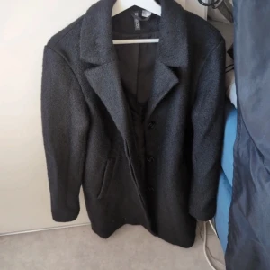 Grå kappa från Zara - Snygg grå kappa från Zara med klassisk design. Den har långa ärmar och knäpps med knappar framtill. Perfekt för kyligare dagar och ger en stilren look.
