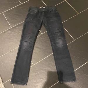 Svarta jeans från Levi's - Snygga svarta Levi's jeans med slitna detaljer på framsidan. Klassisk femficksdesign och en rak passform. Perfekta för en avslappnad stil med en touch av edge.