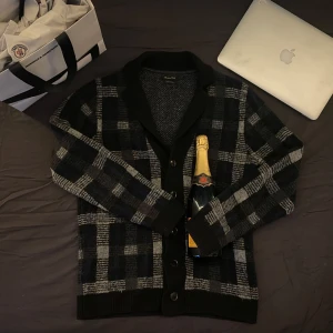 Rutig kofta från Massimo Dutti - Säljer en stilren rutig kofta från Massimo Dutti i svart och grå/blå. Koftan har en klassisk krage och knappar framtill. Perfekt för din garderob.