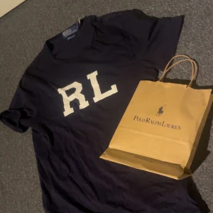  t-shirt Polo Ralph Lauren - Snygg mörkblå t-shirt från Polo Ralph Lauren med stor vit RL-print på bröstet. Modellen är custom slim fit och har korta ärmar. Perfekt för dig som gillar klassisk stil med en modern touch. Materialet är mjuk bomull som känns skönt mot huden.