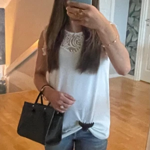 Vit ärmlös blus med spetsdetaljer - Säljer en söt vit blus med ärmlös design och  spetsdetaljer över axlar och även där framme. Toppen har rund halsringning. Passar till både vardag och fest, hör av er om ni har några frågor❤️